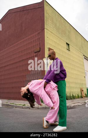 Nicht binäre Person, die eine Frau hält, die sich vor dem Gebäude nach hinten beugt Stockfoto