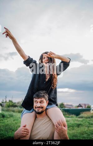 Glücklicher Mann, der Frau auf den Schultern auf dem Land trägt Stockfoto