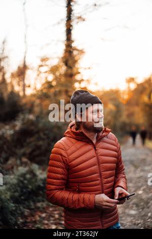 Ein nachdenklicher Mann, der im Wald ein Smartphone hält Stockfoto