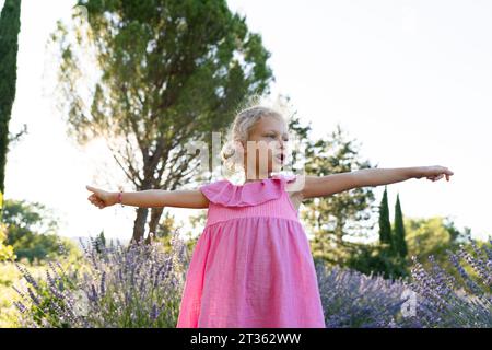 Blondes Mädchen, das mit ausgestreckten Armen im Lavendelfeld steht Stockfoto