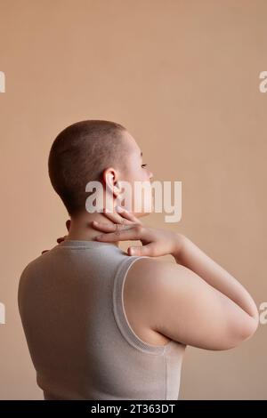 Frau, die den Hals vor beigefarbenem Hintergrund berührt Stockfoto