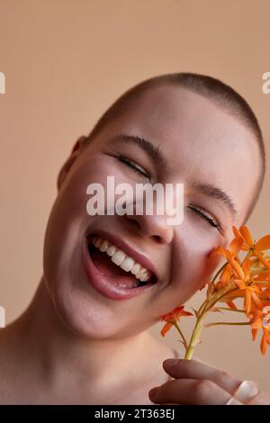 Lachende junge Frau mit Blume vor beigefarbenem Hintergrund Stockfoto