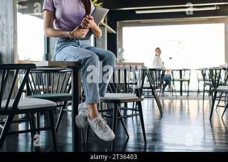 Niedriger Teil einer jungen Frau, die auf dem Kaffeetisch sitzt, mit Laptop in den Händen Stockfoto