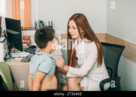 Ärztin untersucht den Herzschlag des Jungen mit Stethoskop in der medizinischen Klinik Stockfoto