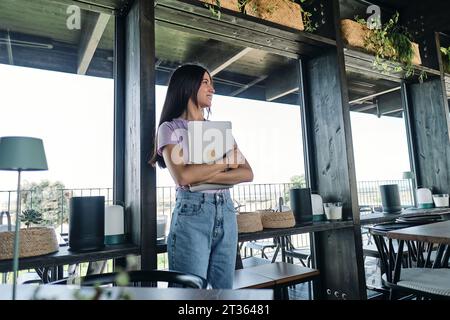 Porträt einer schönen brünetten Frau, die im Café steht, mit Laptop in den Händen Stockfoto