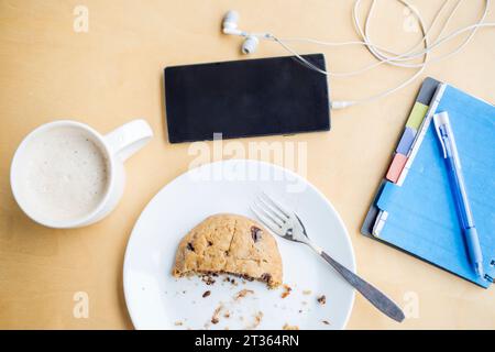 Kaffeetasse mit Keksscheibe auf Teller in der Nähe von Smartphone und Milchküche am Tisch Stockfoto