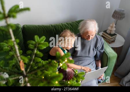 Ältere Frau, die zu Hause ihren Laptop benutzt, mit Enkelin auf dem Sofa Stockfoto