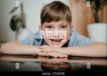 Lächelnder Junge mit Kopf auf den Armen zu Hause Stockfoto
