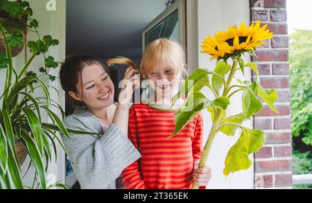 Lächelndes Mädchen mit großer Sonnenblume, die neben Schwester auf dem Balkon steht Stockfoto