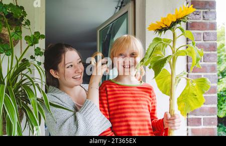 Glückliches Mädchen mit großer Sonnenblume, das bei Schwester auf dem Balkon steht Stockfoto