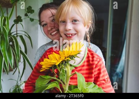 Teenager-Mädchen mit blonder Schwester, die Sonnenblume auf dem Balkon hält Stockfoto