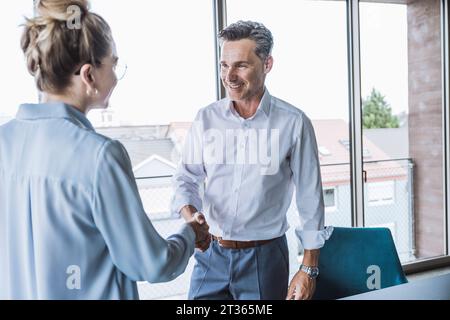 Lächelnd Geschäftsmann Händeschütteln mit Geschäftsfrau im Büro Stockfoto
