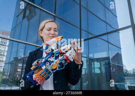 Lächelnde Architektin untersucht Roboterarm in der Nähe von Bürogebäuden Stockfoto