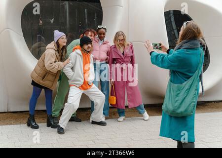 Eine junge Frau, die Selfie von Freunden macht, per Smartphone auf dem Bürgersteig Stockfoto