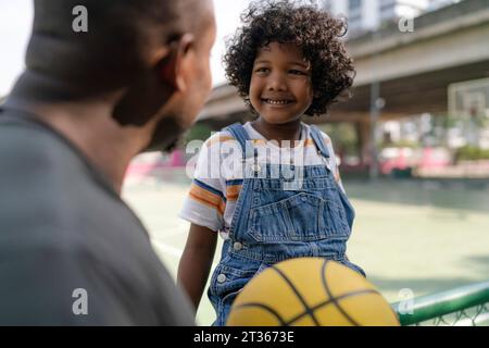 Glücklicher Sohn, der mit Vater auf dem Basketballfeld spricht Stockfoto