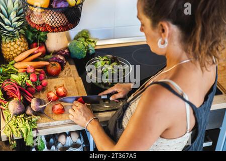 Schwangere Frau, die Tomaten in der Nähe verschiedener Gemüsesorten in der Küche zu Hause schneidet Stockfoto
