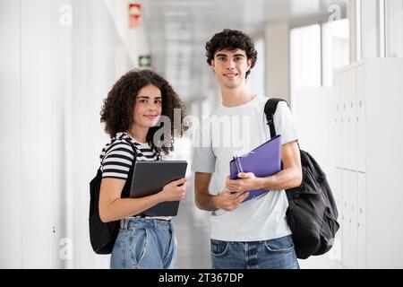 Glückliche Studenten stehen mit Laptop und Aktenordner auf dem Flur Stockfoto