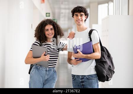 Glückliche Studenten halten Aktenordner und Laptop auf dem Flur Stockfoto