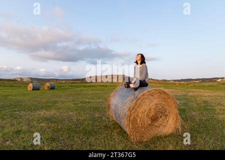 Frau, die auf dem Feld auf Heu sitzt Stockfoto