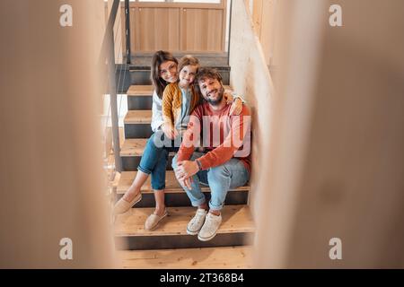 Lächelnder Mann, der mit Frau und Tochter zu Hause auf der Treppe sitzt Stockfoto