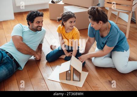 Glückliche Familie, die zu Hause mit Modellhaus auf dem Boden sitzt Stockfoto