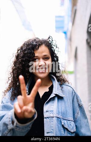 Glückliche junge Frau, die Friedenszeichen zeigt Stockfoto