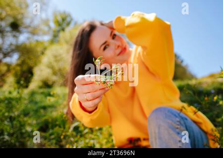 Lächelnde Frau mit Hand im Haar, die Blumen zeigt Stockfoto