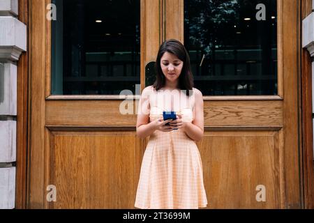 Eine junge Frau, die ein Smartphone vor einer Holztür benutzt Stockfoto