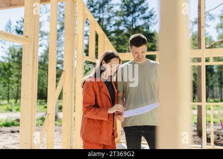 Ein lächelndes Paar, das sich einen Plan ansieht und sich an sonnigen Tagen in der Nähe des Bauwerks unterhalten kann Stockfoto