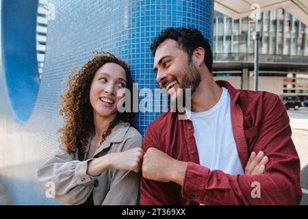 Glücklicher Mann und Frau, die sich die Faust in der Nähe der blauen Mauer anschlagen Stockfoto