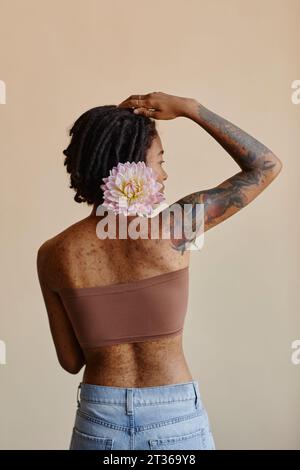 Junge Frau mit kurzen Haaren, die Pfingstrosenblüte vor braunem Hintergrund hält Stockfoto