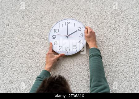 Augsburg, Bayern, Deutschland - 17. Oktober 2023: Mann stellt eine Uhr an der Wand hängend auf die Winterzeit. Zeitänderungskonzept *** Mann stellt eine an der Wand hängende Uhr um auf Winterzeit. Zeitumstellung Konzept Stockfoto