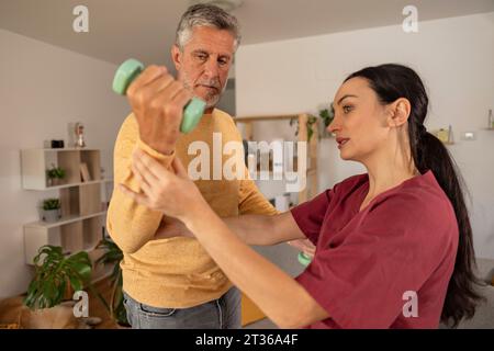 Therapeut unterrichte Übungen an Menschen mit Kurzhanteln zu Hause Stockfoto