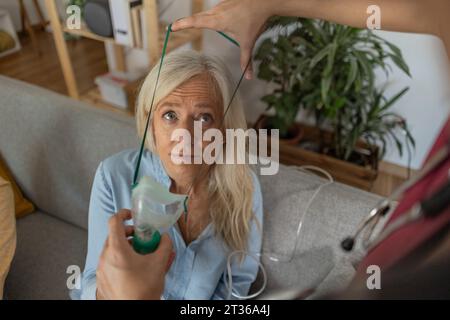 Der Arzt legt zu Hause eine Sauerstoffmaske auf das Gesicht des Patienten Stockfoto