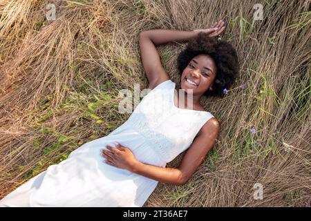 Glückliche junge Frau, die sich auf trockenem Gras auf dem Feld entspannt Stockfoto