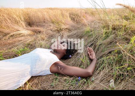 Frau mit geschlossenen Augen, die sich auf trockenem Gras auf dem Feld entspannt Stockfoto