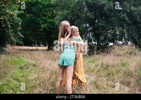 Glückliches Mädchen, das Mutter umarmt und auf trockenem Gras im Park steht Stockfoto