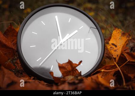 Gersthofen, Bayern, Deutschland. Oktober 2023. Schwarze Uhr auf einem Stapel mit Herbstlaub. Zeitwechsel im Herbstkonzept *** schwarze Runde Uhr in einem Haufen mit Herbstlaub. Zeitumstellung im Herbst Konzept Credit: Imago/Alamy Live News Stockfoto