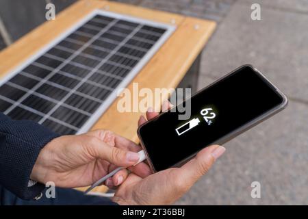 Hände einer Geschäftsfrau, die ihr Smartphone mit Solarstrom auf der Bank auflädt Stockfoto