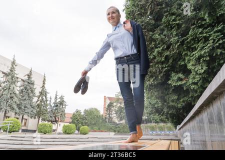 Sorglose Geschäftsfrau, die auf der Bank im Park balanciert Stockfoto