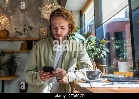 Geschäftsmann, der das Smartphone benutzt und sich auf den Schreibtisch im Café lehnt Stockfoto