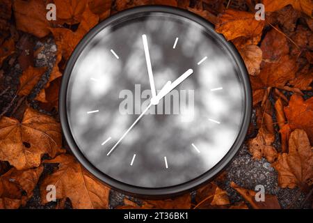 Gersthofen, Bayern, Deutschland. Oktober 2023. Schwarze Uhr auf einem Stapel mit Herbstlaub. Zeitwechsel im Herbstkonzept *** schwarze Runde Uhr in einem Haufen mit Herbstlaub. Zeitumstellung im Herbst Konzept Credit: Imago/Alamy Live News Stockfoto