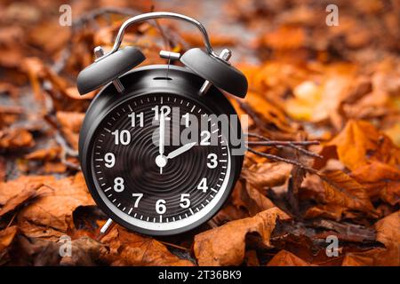 Gersthofen, Bayern, Deutschland. Oktober 2023. Zeitumstellung von Sommerzeit auf Winterzeit, Ein schwarzer Wecker mitten im Herbst verlässt mit der Zeit 2 Uhr *** Zeitumstellung von Sommerzeit auf Winterzeit, ein schwarzer Wecker inmitten von Herbstlaub mit der Zeit 2 Uhr Credit: Imago/Alamy Live News Stockfoto