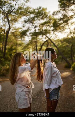 Mutter flechtet die Haare der Tochter, die auf der Straße im Wald steht Stockfoto