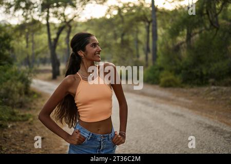 Lächelndes Teenager-Mädchen mit Händen in Taschen bei Sonnenuntergang Stockfoto