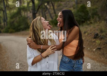 Glückliche Mutter und Tochter, die sich anschauen und Zungen im Wald ausstrecken Stockfoto