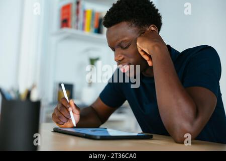 Junger Student, der am Schreibtisch auf einem Tablet-PC studiert und schreibt Stockfoto