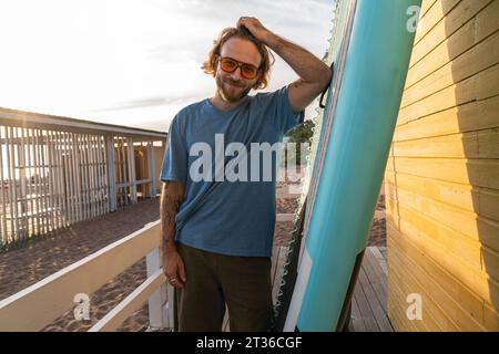 Lächelnder Mann mit Hand im Haar, der in der Nähe der Strandhütte steht Stockfoto
