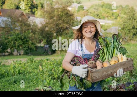 Lächelnde Frau mit Wurzelgemüse in der Kiste im Garten Stockfoto