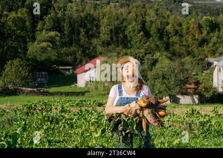 Frau mit Hut und Karotten auf dem Feld an sonnigem Tag Stockfoto